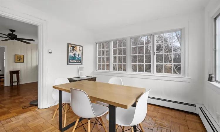 Small sitting space with table located in the sun room, featuring a baseboard heating unit, ceiling fan, and parquet floors