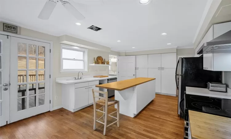 Kitchen with white cabinetry, light wood-type flooring, a kitchen island, a breakfast bar, and sink