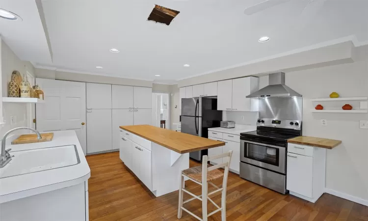 Kitchen featuring appliances with stainless steel finishes, ornamental molding, white cabinetry, and wall chimney range hood