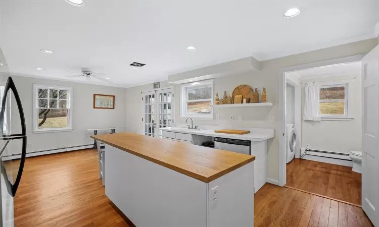 Kitchen with stainless steel dishwasher, a baseboard heating unit, white cabinetry, and light hardwood / wood-style flooring