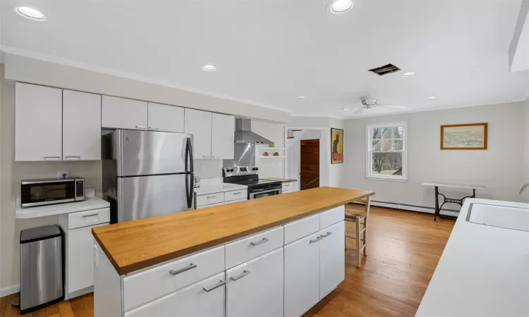 Kitchen featuring wall chimney range hood, a kitchen island, sink, white cabinetry, and stainless steel appliances