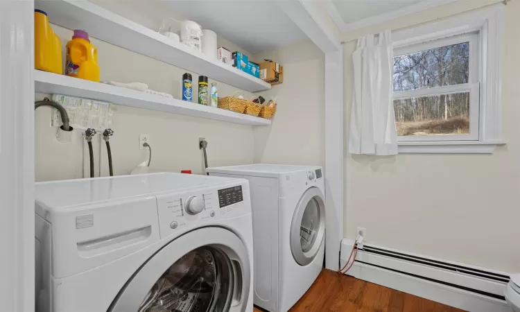 Clothes washing area featuring baseboard heating, dark hardwood / wood-style flooring, crown molding, and washing machine and clothes dryer