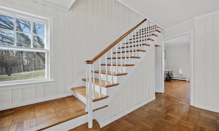 Staircase featuring a baseboard heating unit, ornamental molding, and parquet flooring