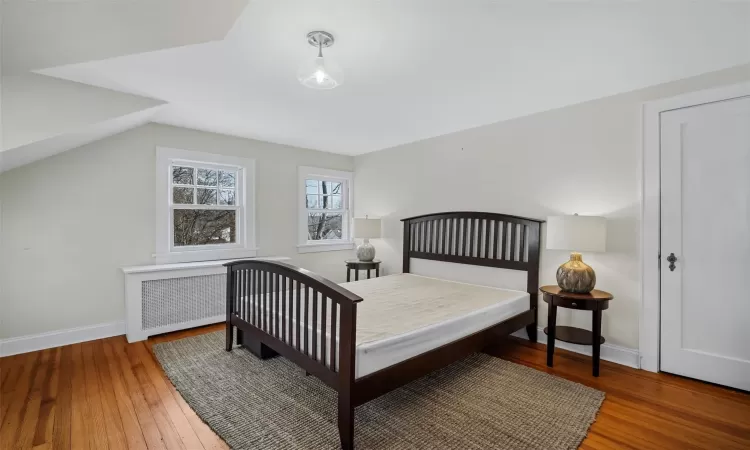 Bedroom with hardwood / wood-style floors, radiator heating unit, and lofted ceiling