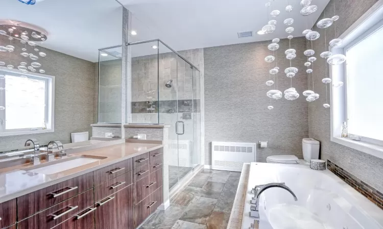 Full bathroom with radiator heating unit, toilet, vanity, and separate shower and tub