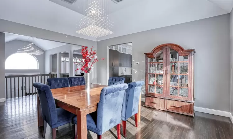 Dining space with sink, vaulted ceiling, a notable chandelier, and dark hardwood / wood-style flooring