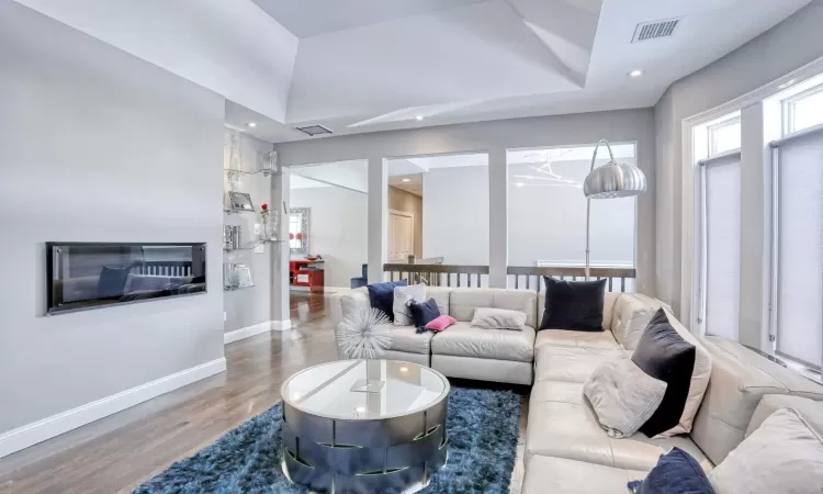 Living room with hardwood / wood-style flooring, a tray ceiling, and lofted ceiling