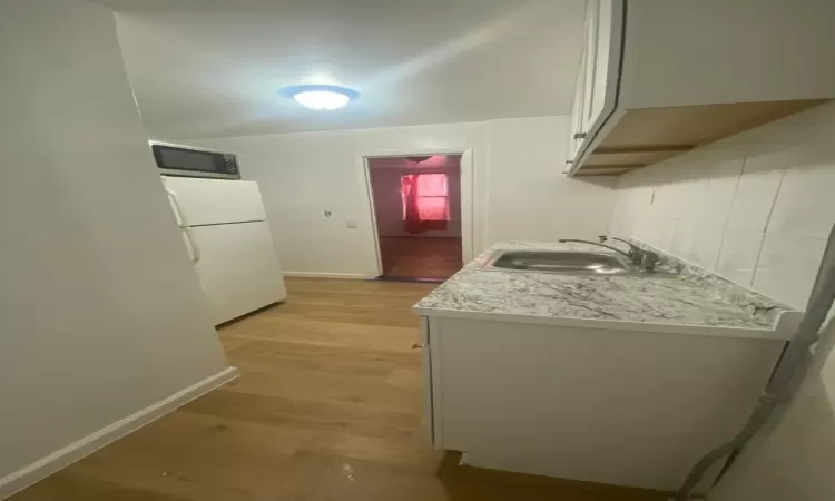 Kitchen with white cabinetry, sink, light hardwood / wood-style flooring, and white fridge