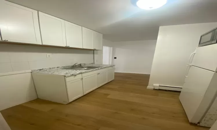 Kitchen featuring a baseboard radiator, sink, white cabinets, and light hardwood / wood-style floors