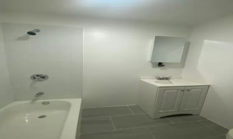 Bathroom with tile patterned floors, tiled shower / bath combo, and vanity