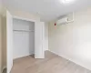 Unfurnished bedroom featuring a wall mounted AC, light hardwood / wood-style floors, and a closet