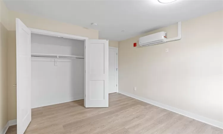 Unfurnished bedroom featuring a wall mounted AC, light hardwood / wood-style floors, and a closet