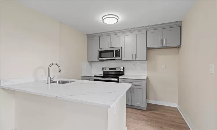 Kitchen with sink, stainless steel appliances, light stone counters, tasteful backsplash, and kitchen peninsula