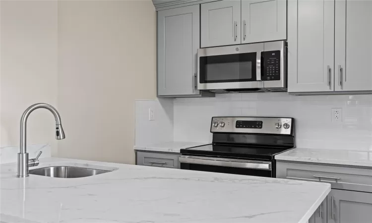 Kitchen featuring stainless steel appliances, sink, gray cabinetry, and light stone counters