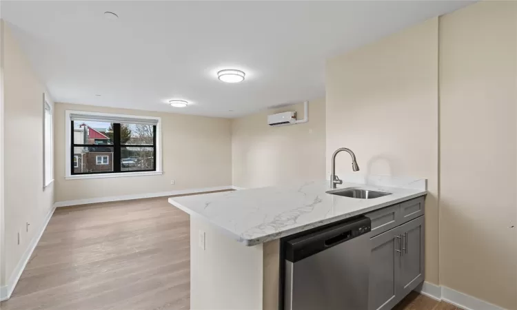 Kitchen featuring sink, light hardwood / wood-style flooring, dishwasher, light stone counters, and an AC wall unit