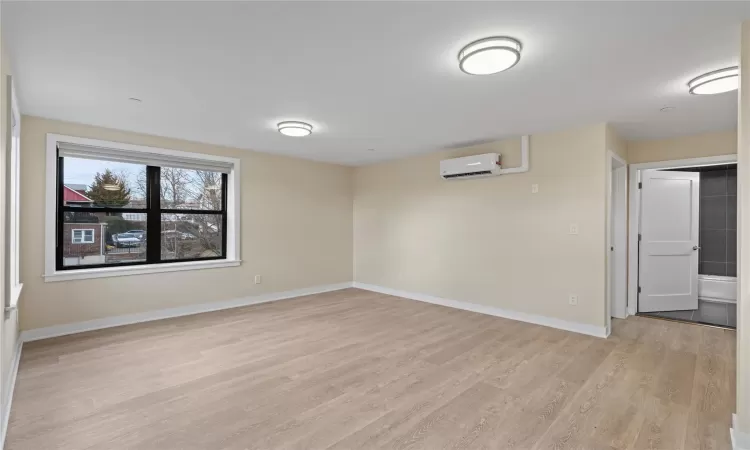 Empty room with light hardwood / wood-style floors and a wall unit AC