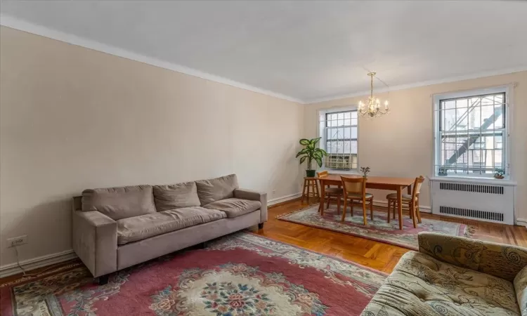 Living room with ornamental molding, parquet flooring, radiator heating unit, and a chandelier