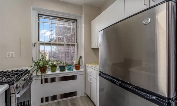 Kitchen featuring stainless steel appliances, white cabinetry, radiator, and light hardwood / wood-style floors