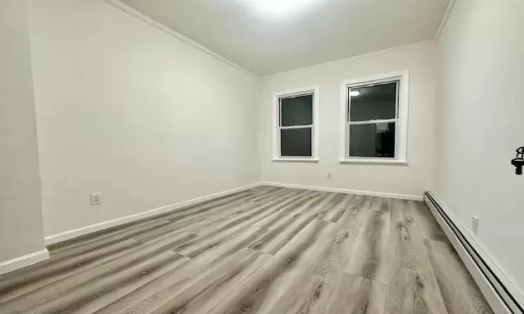 Spare room featuring crown molding, light wood-type flooring, and a baseboard heating unit