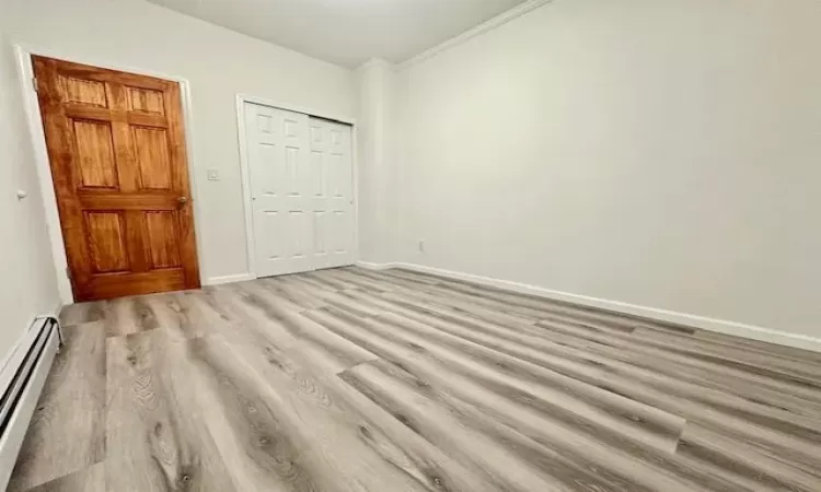 Unfurnished bedroom featuring crown molding, light hardwood / wood-style floors, a closet, and a baseboard heating unit