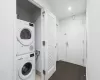 Washroom with stacked washer / drying machine and dark hardwood / wood-style floors