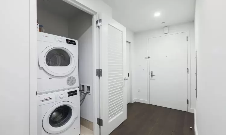 Washroom with stacked washer / drying machine and dark hardwood / wood-style floors