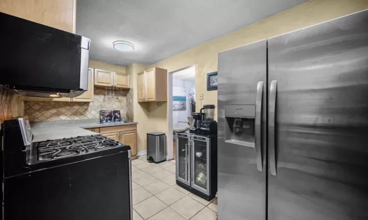 Kitchen with range with gas cooktop, tasteful backsplash, light tile patterned floors, stainless steel refrigerator with ice dispenser, and light brown cabinets