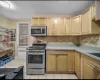 Kitchen featuring light tile patterned flooring, appliances with stainless steel finishes, radiator, and light brown cabinetry