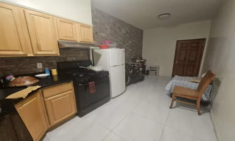 Kitchen with tasteful backsplash, light tile patterned floors, white refrigerator, and black gas range