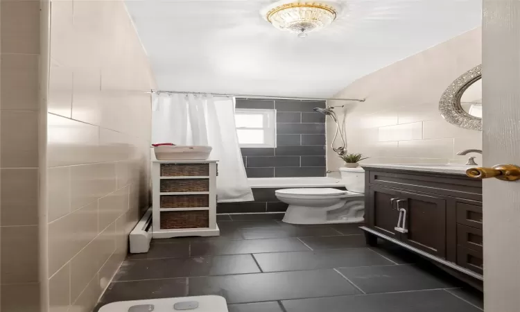 Full bathroom featuring a baseboard radiator, tile walls, vanity, toilet, and shower / bath combo