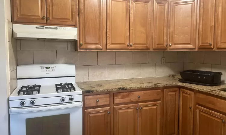 Kitchen with backsplash, light stone counters, and white gas range