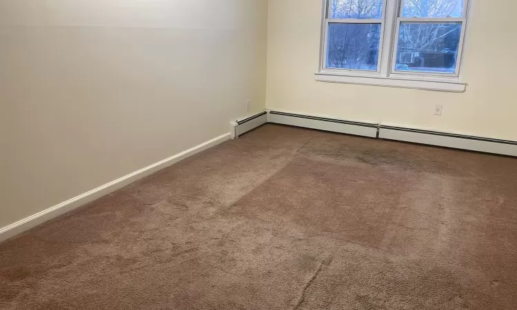 Carpeted empty room featuring baseboard heating