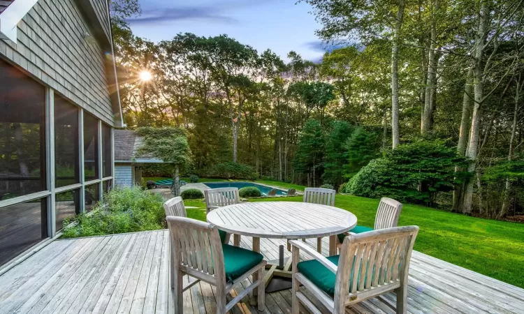 Deck at dusk with a sunroom, a yard, and a swimming pool