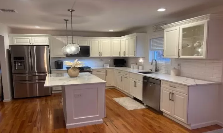 Kitchen with sink, white cabinets, hanging light fixtures, a center island, and stainless steel appliances