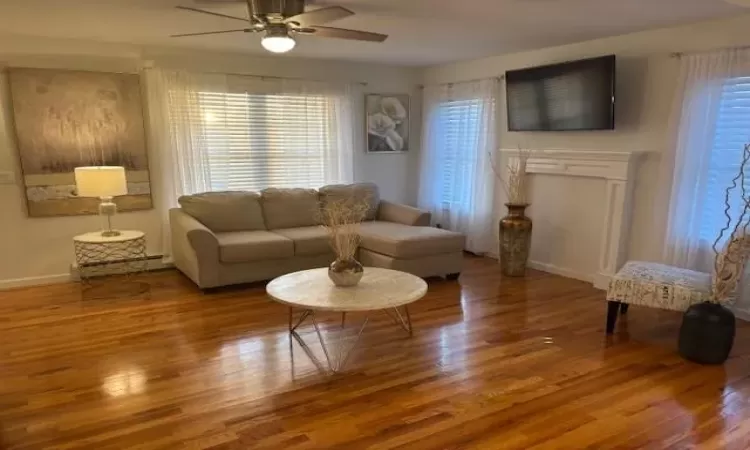 Living room with hardwood / wood-style flooring, a baseboard radiator, and ceiling fan