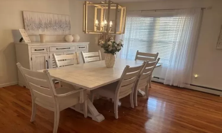 Dining room with a baseboard radiator, dark hardwood / wood-style floors, and a notable chandelier