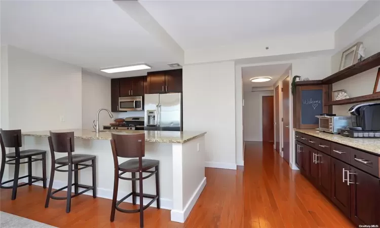 Kitchen featuring appliances with stainless steel finishes, a kitchen bar, light stone counters, kitchen peninsula, and light hardwood / wood-style floors