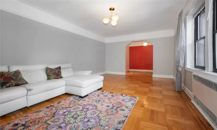 Living room featuring a healthy amount of sunlight, radiator, parquet floors, and a notable chandelier