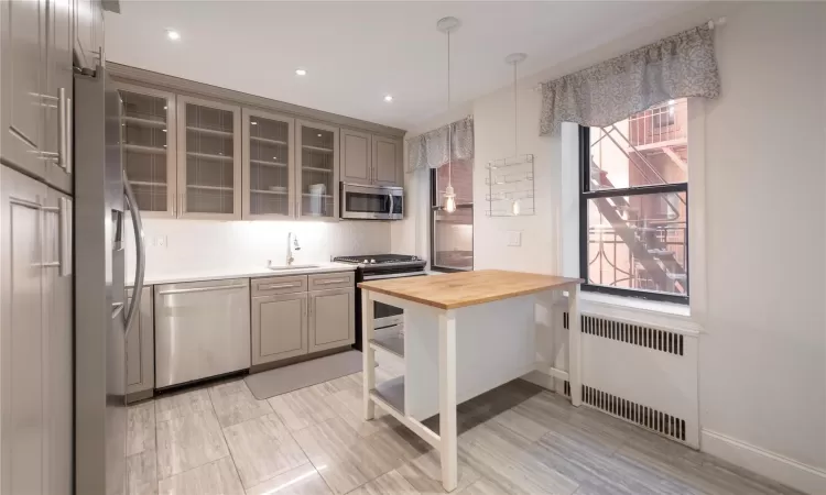 Kitchen featuring pendant lighting, butcher block countertops, radiator, sink, and stainless steel appliances