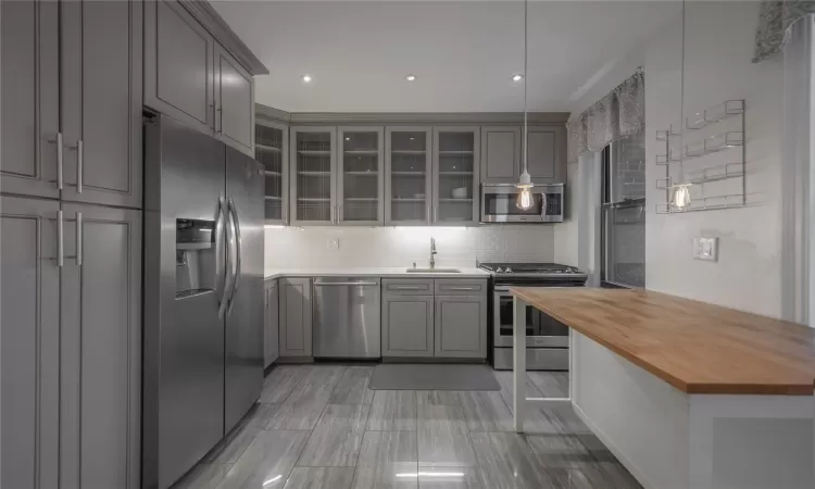 Kitchen with sink, wooden counters, appliances with stainless steel finishes, gray cabinetry, and tasteful backsplash