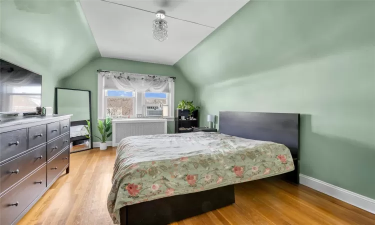 Bedroom with lofted ceiling, radiator, light hardwood / wood-style floors, and multiple windows