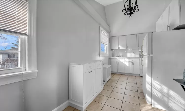 Kitchen with white refrigerator, plenty of natural light, hanging light fixtures, and white cabinets