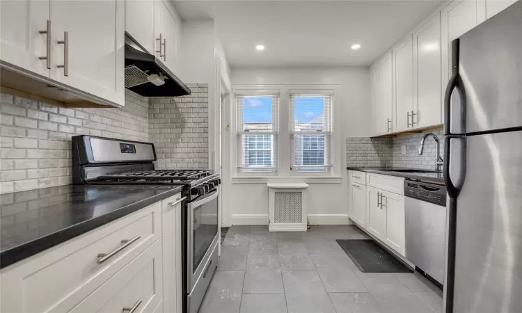 Kitchen with sink, white cabinets, backsplash, light tile patterned floors, and stainless steel appliances