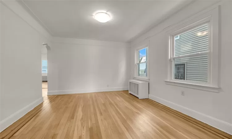 Empty room with crown molding, radiator, and light hardwood / wood-style flooring