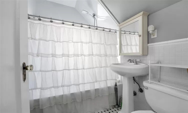 Bathroom with vaulted ceiling, tile walls, a shower with shower curtain, and toilet