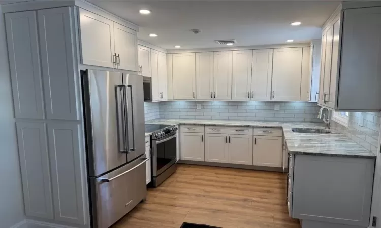 Kitchen featuring white cabinetry, wood-type flooring, sink, light stone counters, and stainless steel appliances