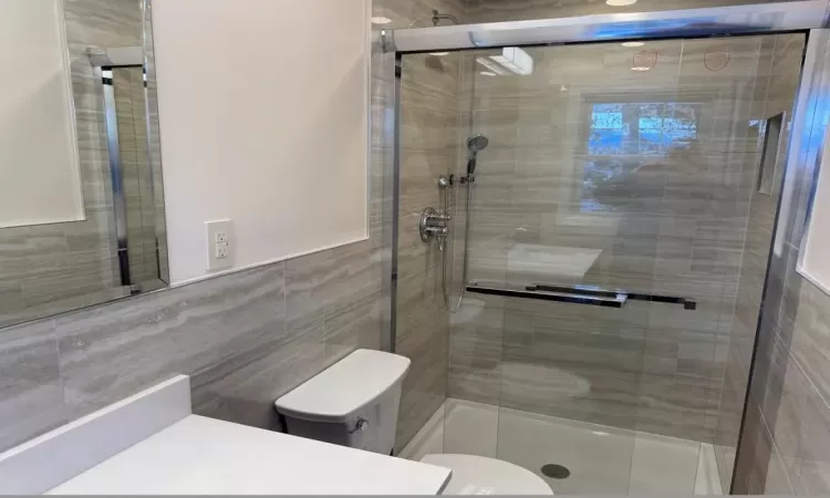 Bathroom with toilet, a shower with shower door, and tile walls