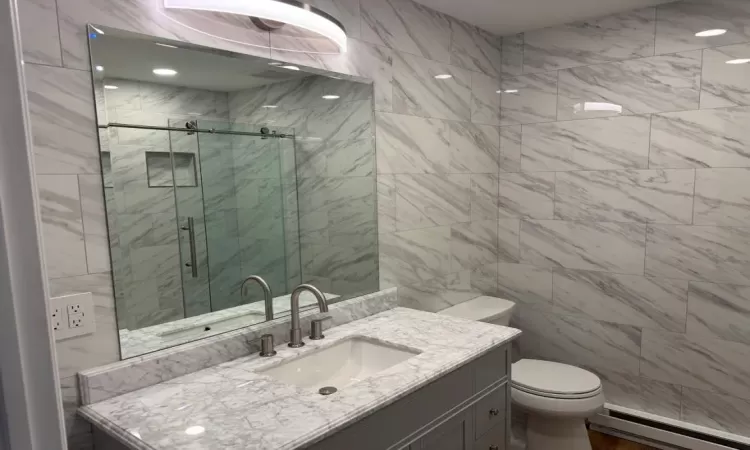 Bathroom featuring a shower with door, a baseboard radiator, vanity, and toilet