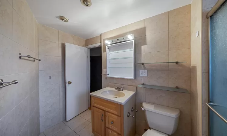 Bathroom featuring toilet, tile walls, tile patterned floors, vanity, and radiator heating unit