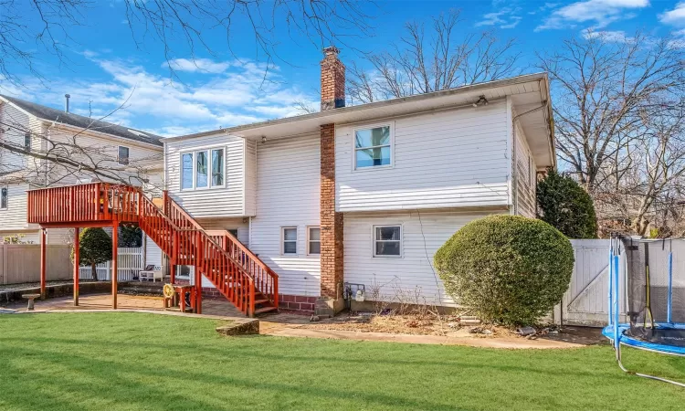 Back of property featuring a lawn, a trampoline, and a wooden deck